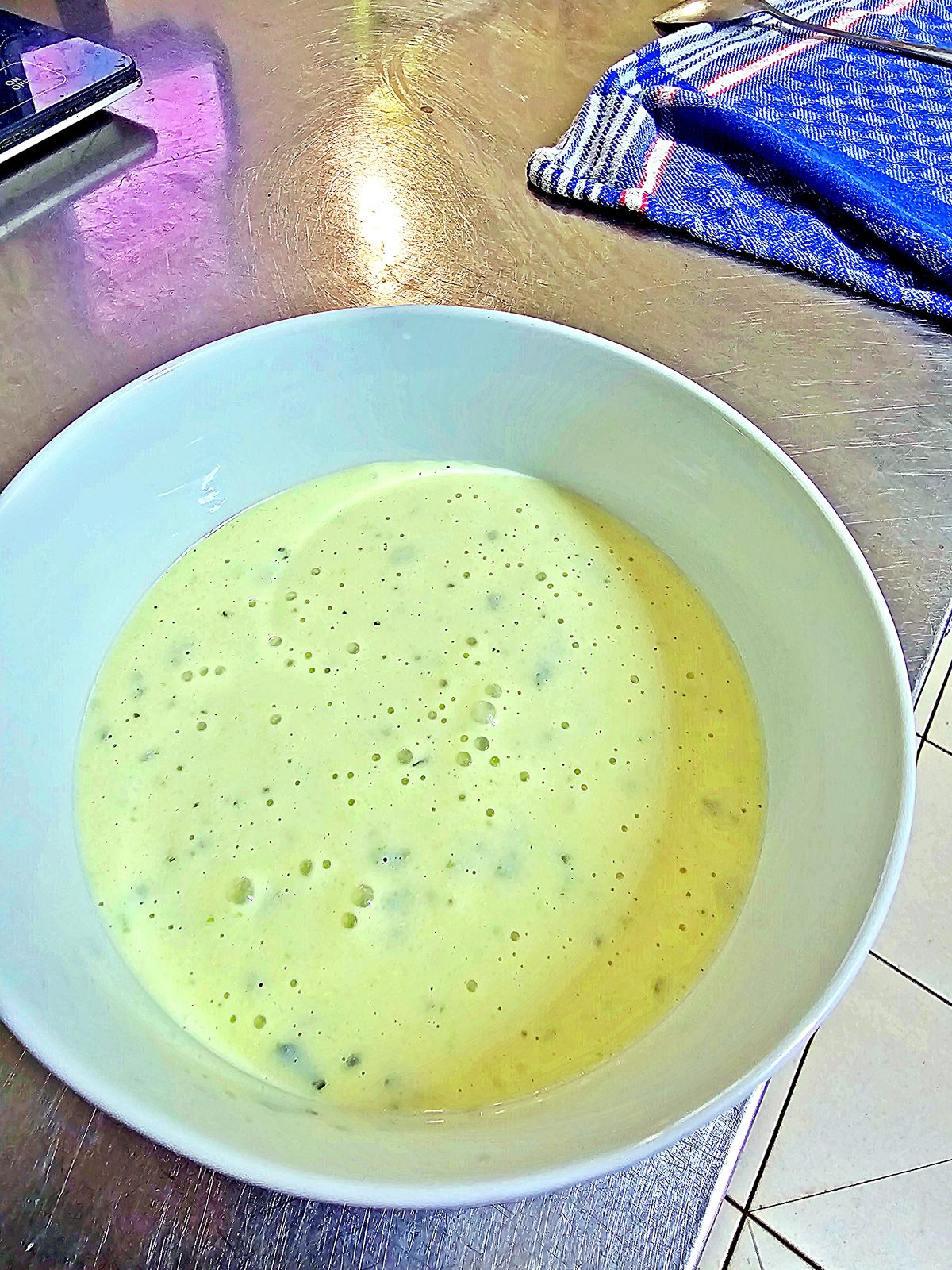 Cucumber cold soup made with soy yoghurt in a white bowl on a steel kitchen worktop